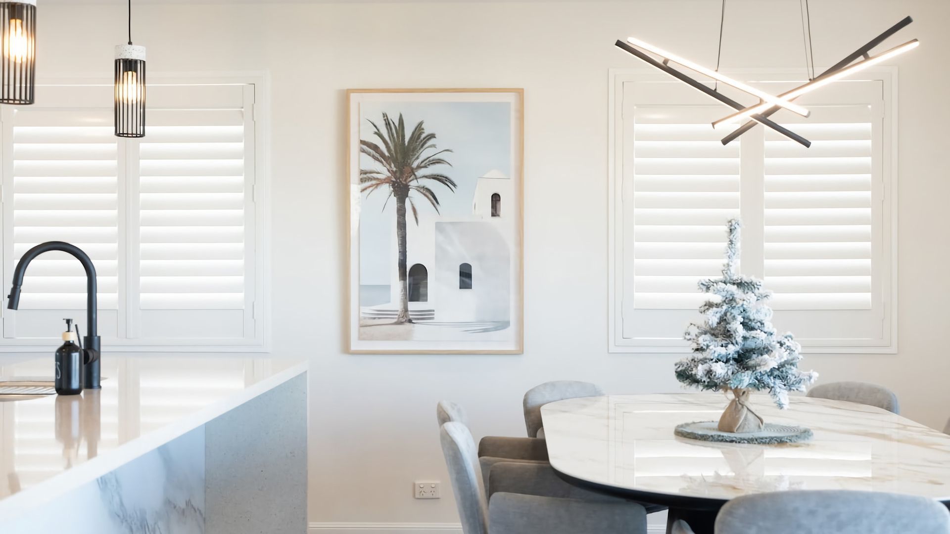 Uma sala de jantar moderna com uma mesa redonda, cadeiras, uma pequena árvore de Natal e um quadro na parede.