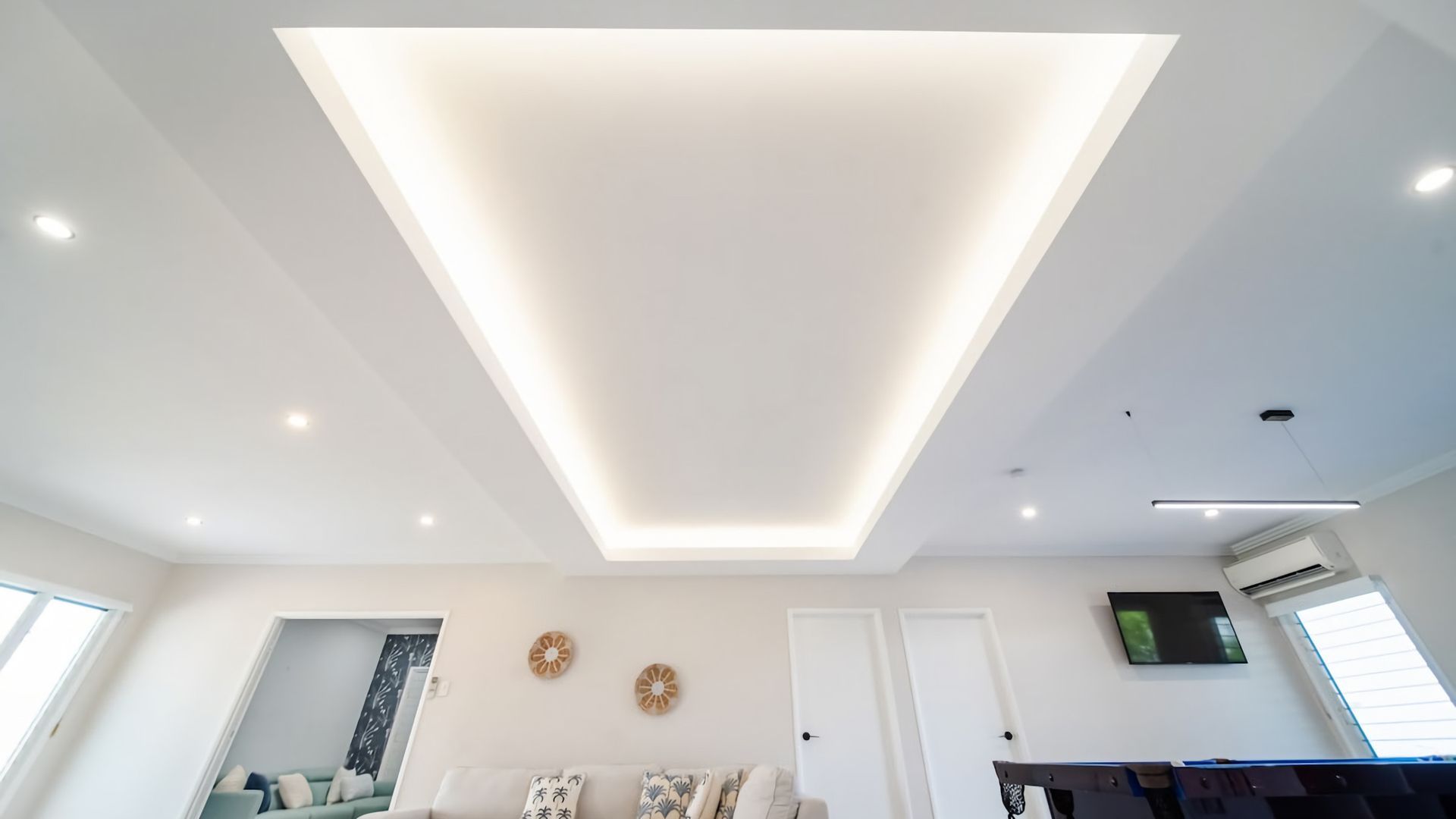 A modern living room with a recessed ceiling light, a sofa, a television, and a door.