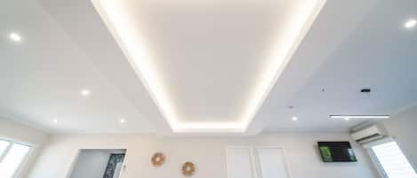 A modern living room with a recessed ceiling light, a sofa, a television, and a door.
