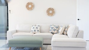 A modern living room with a white sofa, two decorative wall pieces, and a green ottoman. - Executive Coastal Living with Ocean Views (Bushland Beach)