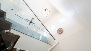 A modern interior with a glass railing, a geometric light fixture, and a decorative plate on the wall. - Executive Coastal Living with Ocean Views (Bushland Beach)