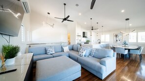 A modern living space with a sectional sofa, a dining area, and a kitchen. - Executive Coastal Living with Ocean Views (Bushland Beach)
