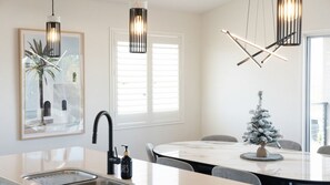 A modern kitchen with a marble countertop, a sink, and a faucet. There is a Christmas tree on the dining table. - Executive Coastal Living with Ocean Views (Bushland Beach)