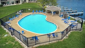 En swimmingpool med træterrasse, omgivet af et sort hegn, og blå liggestole.