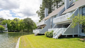 A waterfront property with a grassy lawn, a dock, and a building with a balcony. - Lakefront Sea Colony condo; private beach access (South Bethany)