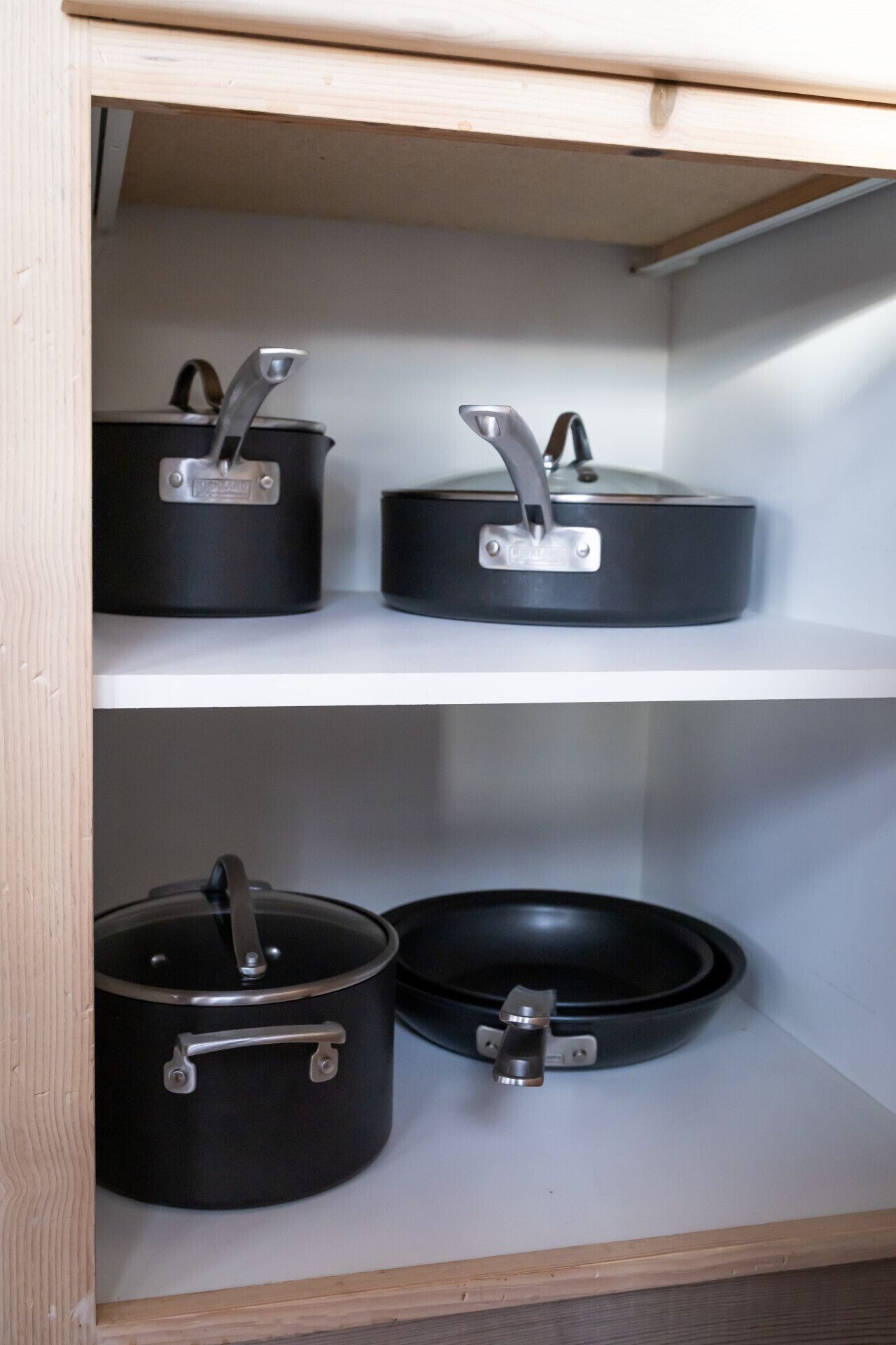 Un meuble en bois doté de trois étagères, chacune contenant un pot noir muni d’une anse en métal.