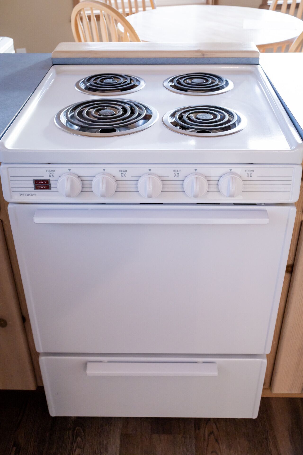 A white Premier range cooker with four burners and a front oven, located in a kitchen with wooden cabinets and a dining table in the background.