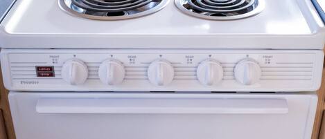 A white Premier range cooker with four burners and a front oven, located in a kitchen with wooden cabinets and a dining table in the background.