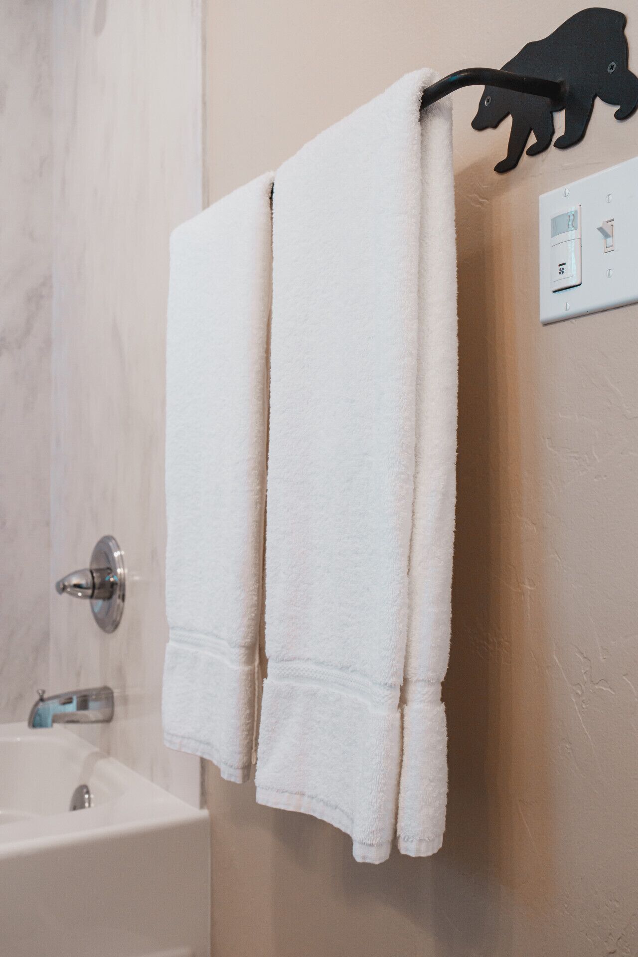 A bathroom with a white towel hanging on a towel rack, a black bear-shaped towel holder, and a wall-mounted thermostat.