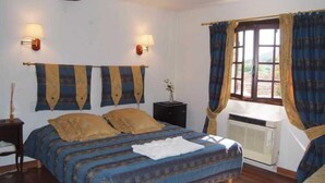 A bedroom with a bed, two wall-mounted lamps, a window with curtains, and an air conditioning unit. - Le Logis du Guetteur (Les Arcs-sur-Argens)
