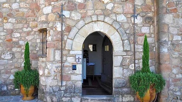 A stone building entrance with an arched doorway, two potted plants, and a small sign on the wall. - Le Logis du Guetteur (Les Arcs-sur-Argens)