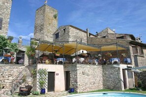 A stone building with a tower, outdoor seating area, and a pool. - Le Logis du Guetteur (Les Arcs-sur-Argens)