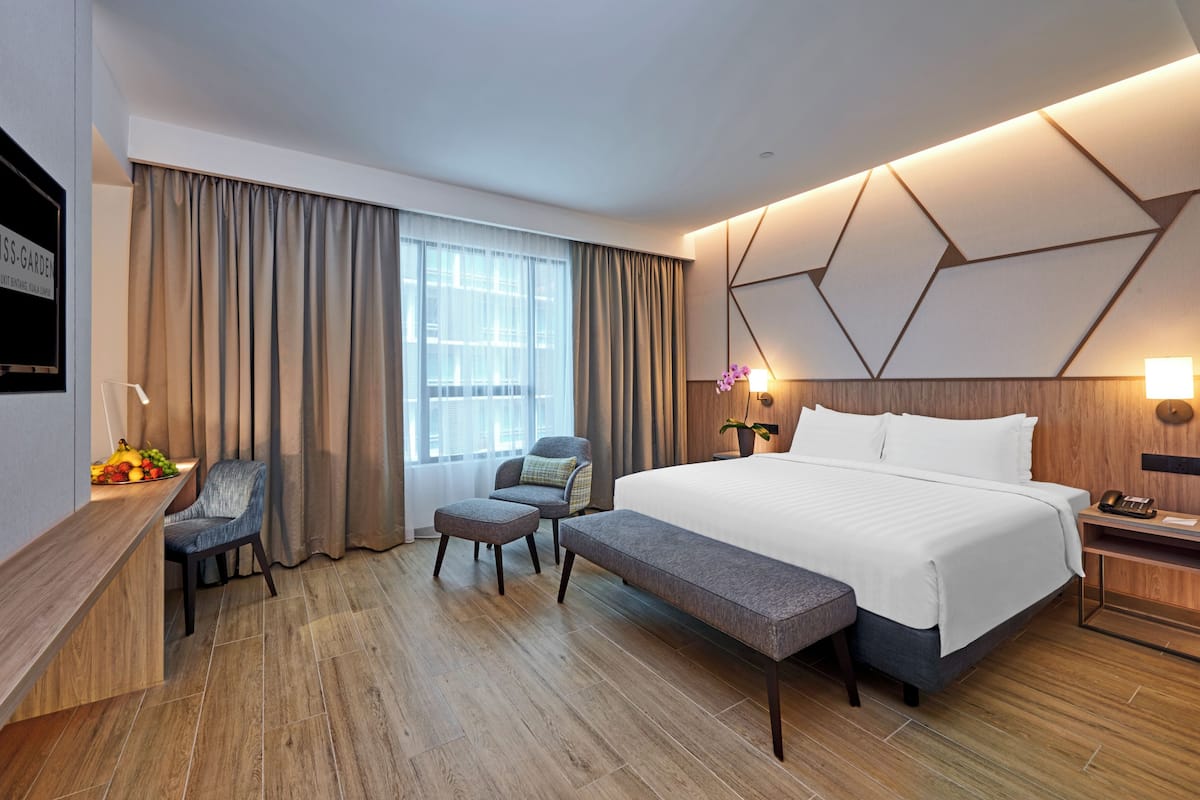 Ein modernes Hotelzimmer mit einem großen Bett, einem Schreibtisch mit Obstschale, einem Sessel und einer Bank.