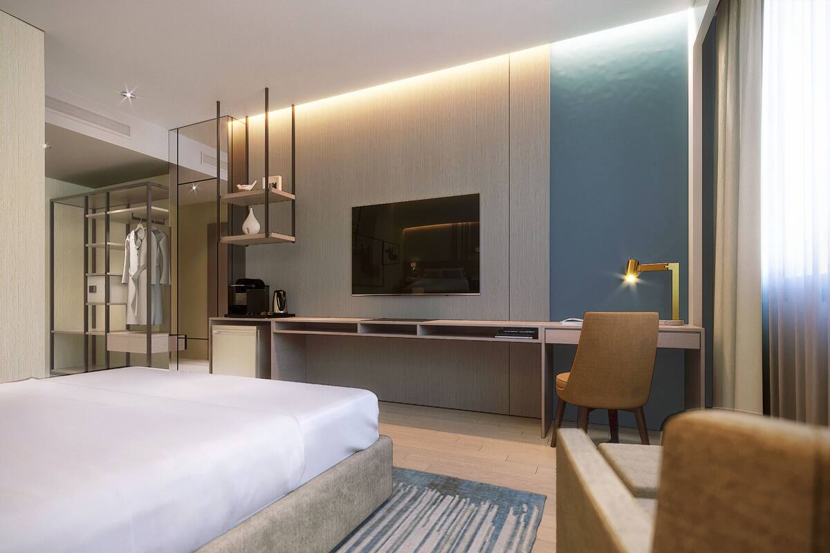 Ein modernes Hotelzimmer mit einem großen Bett, einem Schreibtisch mit Stuhl, einem Fernseher und einem Kleiderschrank.