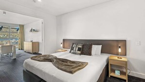 A modern hotel room with a large bed, bedside tables, a desk, and a view of the outside. - Family-Friendly 3BR Marina Views & Space (Queenstown)
