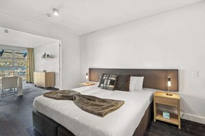 A modern hotel room with a large bed, bedside tables, a desk, and a view of the outside. - Family-Friendly 3BR Marina Views & Space (Queenstown)