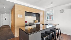 A modern kitchen with a central island, wooden cabinets, stainless steel appliances, and a window with blinds. - Family-Friendly 3BR Marina Views & Space (Queenstown)