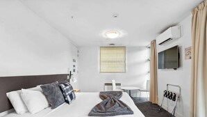 A hotel room with a bed, a desk, a chair, a TV, an air conditioning unit, and a window with curtains. - Lakeside Studio Retreat (Queenstown)