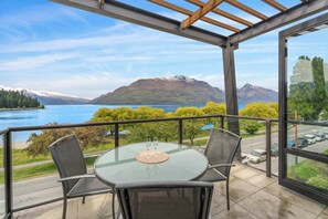A glass table with four chairs on a balcony overlooking a lake and mountains. - Gorgeous Lakefront, 3 Bed apartment, walk to town (Queenstown)
