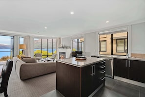A modern kitchen with dark cabinetry, a central island, and a view of the outdoors. - Gorgeous Lakefront, 3 Bed apartment, walk to town (Queenstown)