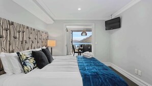 A hotel room with a large bed, a desk, a chair, a TV, and a view of the mountains. - Gorgeous Lakefront, 3 Bed apartment, walk to town (Queenstown)