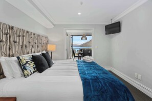 A hotel room with a large bed, a desk, a chair, a TV, and a view of the mountains. - Gorgeous Lakefront, 3 Bed apartment, walk to town (Queenstown)