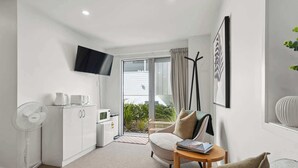 Ein modernes Wohnzimmer mit einer Couch, einem kleinen Tisch, einem an der Wand montierten Fernseher und einer Schiebeglastür, die auf einen Balkon führt.