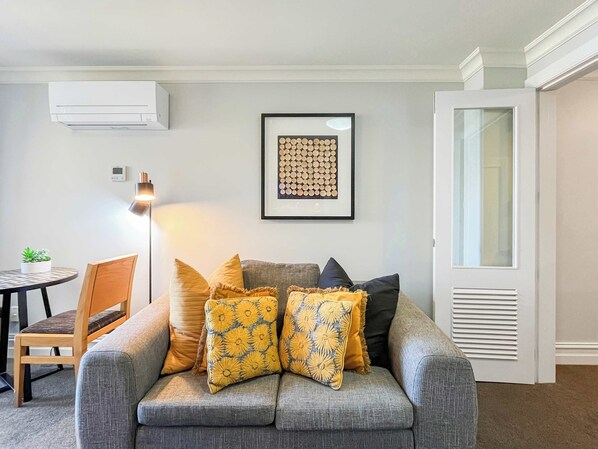 A living room with a grey sofa, yellow and black patterned cushions, a framed artwork on the wall, and a white door. - Lakefront Central Studio, walk to town! (Queenstown)