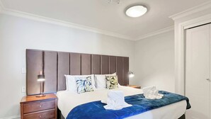 Ein Hotelzimmer mit einem großen Bett, einem Nachttisch aus Holz, einem Schreibtisch und einem Kleiderschrank.
