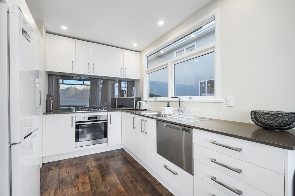 A modern kitchen with white cabinets, stainless steel appliances, a large window, and a view of mountains.