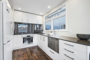 A modern kitchen with white cabinets, stainless steel appliances, a large window, and a view of mountains. - The Biggest & Best Views, 3 Bedrooms, Walk To Town (Queenstown)