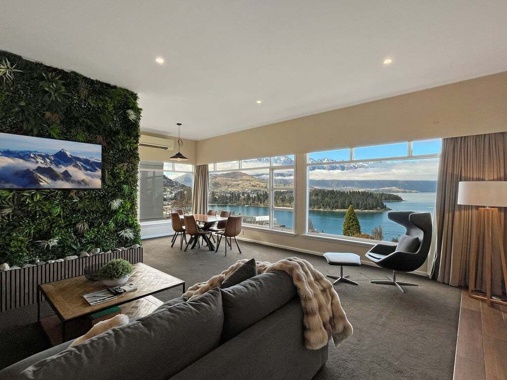 A modern living room with a large window, a green wall, and a view of a lake and mountains.