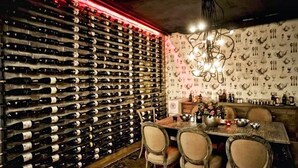A wine cellar with a wall of wine bottles, a dining table with chairs, and a chandelier. - Tunel Residence (Istanbul)