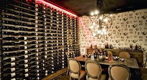 A wine cellar with a wall of wine bottles, a dining table with chairs, and a chandelier. - Tunel Residence (Istanbul)