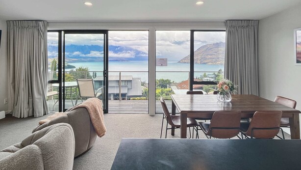 A modern hotel room with a large sliding glass door leading to a balcony with a scenic ocean view. - Quiet Home with Stunning Lake & Mountain Views (Queenstown)