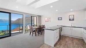 A modern kitchen with a large island, white cabinetry, and a view of the sea through large sliding doors. - Quiet Home with Stunning Lake & Mountain Views (Queenstown)