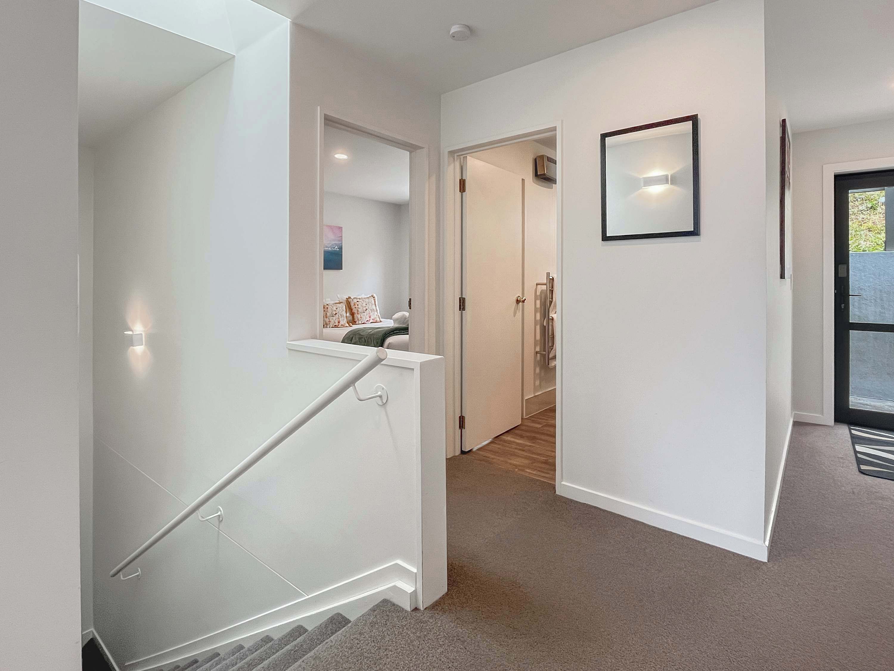 A modern interior with a staircase, a hallway leading to a bathroom, and a door leading outside.