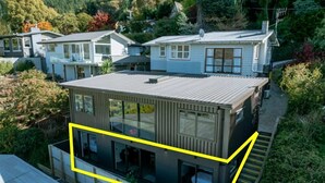 A modern two-story house with a flat roof, large windows, and a visible staircase leading to the upper floor. - Central Charm | 10 Min Walk to CBD (Queenstown)