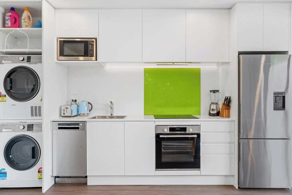 A compact kitchen with a washing machine, microwave, oven, and refrigerator.