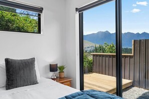 Ein Schlafzimmer mit einem Bett, einem Nachttisch, einer Lampe und Blick auf Berge durch eine Schiebetür.