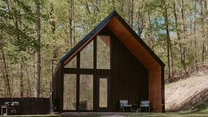 A wooden cabin with large windows, a porch, and a stone pathway leading to it. - The Kinky Cabin Adult Themed A-Frame (Walker County)