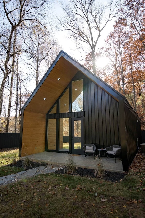 Una casa moderna con un amplio ventanal, revestimiento de madera y un patio con dos sillas.