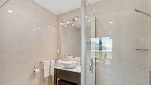 Un baño moderno con ducha de vidrio, lavamanos blanco y retrete.