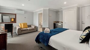 Una habitación de hotel con cama, sofá, escritorio y baño visible a través de una puerta abierta.
