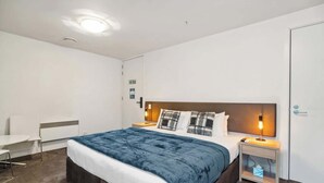 Ein modernes Hotelzimmer mit Bett, Nachttischen, einem Schreibtisch und einem Fluchtwegschild.
