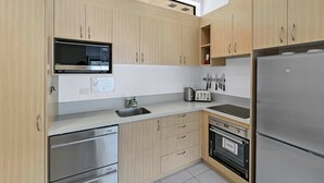 Une cuisine moderne avec des meubles en bois clair, des appareils en acier inoxydable, un four à micro-ondes encastré et un grille-pain.