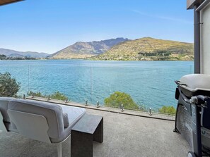 Een balkon met uitzicht op een meer en bergen, een grijze bank en een barbecue.