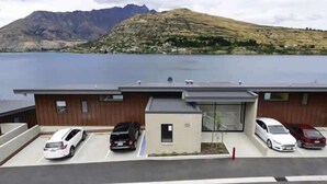 Un bâtiment moderne avec un espace de stationnement à l’avant, offrant une vue sur un lac et des montagnes.