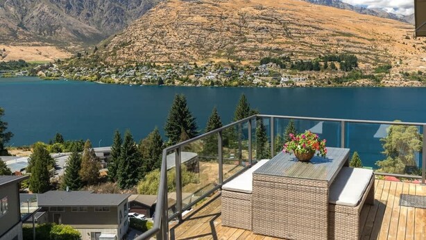Un balcón con un sofá de mimbre y una maceta con flores, con vistas a un lago y montañas.