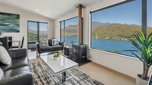 Una sala de estar moderna con chimenea, ventanas amplias y vista a un lago y montañas.